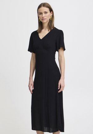 Musta mekko, jossa on lyhyet, hulmuavat hihat, V-pääntie ja virtaava silhouette. Valmistettu teksturoidusta kankaasta, ulottuu puoliväliin säärtä.