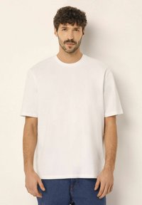 Hvid kortærmet t-shirt med rund halsudskæring, glat tekstur og afslappet pasform, parret med blå denim jeans. Enkel design uden mønstre.