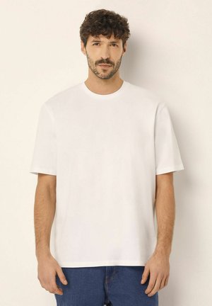 Weiße Kurzarm-T-Shirt mit Rundhalsausschnitt, glatter Textur und lässiger Passform, kombiniert mit blauen Jeans. Einfaches Design ohne Muster.