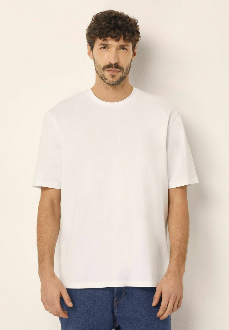 Hvid kortærmet t-shirt med rund halsudskæring, glat tekstur og afslappet pasform, parret med blå denim jeans. Enkel design uden mønstre.
