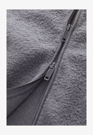 Grijze fleece stof met een zachte textuur en ritsen langs de opening. De ritsen hebben metalen haken langs de randen voor functionaliteit.