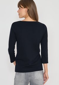 Maglia a maniche lunghe blu navy in tessuto morbido, con scollatura rotonda e vestibilità comoda. Abbinate a jeans grigi chiari.