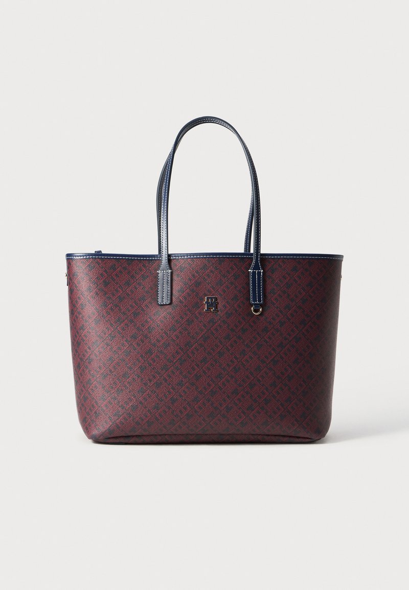 Sac tote rouge et marine en matériau synthétique texturé, doté de deux poignées et d'un logo sur le devant, avec une forme rectangulaire structurée.