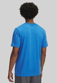 Camiseta de algodón azul con mangas cortas. Presenta un cuello redondo y un pequeño logo en la parte superior de la espalda. Textura suave, corte relajado.