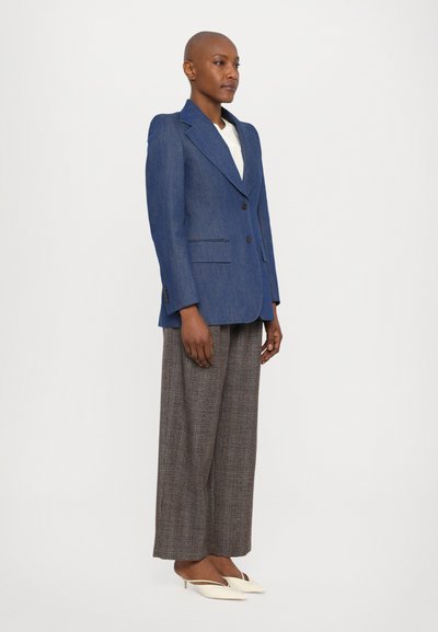 Dark blue tailored blazer with a notched collar, two buttons, and front pockets, paired with brown plaid wide-leg trousers and white pointed shoes.
