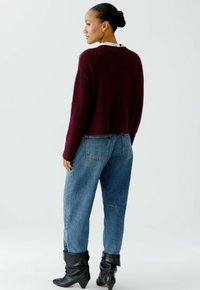 Bordeaux kleurige cropped trui met geribbelde details, gecombineerd met losse blauwe denim jeans en zwarte enkellaarsjes met een ge gathered textuur.