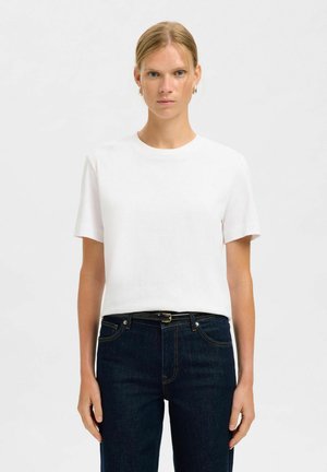 T-shirt en coton blanc à manches courtes, col rond et coupe relaxe, associé à un jean en denim bleu foncé et une ceinture noire. Texture lisse.