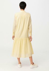 Żółta sukienka z długimi rękawami, z marszczonym tyłem i falbanistym dołem, wykonana z lekkiego materiału. Połączona z białymi trampkami.