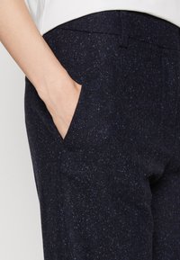 Námořnické modré kalhoty s texturou, které mají jemný tečkovaný vzor, s viditelnou boční kapsou a plochým designem pásku.