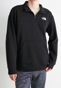 Pullover in pile nero con colletto a zip a un quarto, tasca frontale e polsini e orlo a costine. Presenta un logo bianco sul petto.