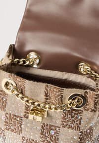 Μικρή τσάντα ώμου σε μπεζ και καφέ σχέδιο, με χρυσή αλυσίδα, λεπτομέρειες με στρας και χρυσό κλείδωμα, μισάνοιχτη για να φαίνεται το λείο εσωτερικό ύφασμα.