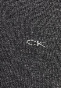 Grå strikket sok med en struktureret overflade, der har et lille hvidt "CK" logo broderet på siden.