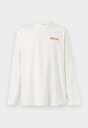 Bela majica z dolgimi rokavi z oranžnim logotipom "Just Cavalli" na levi strani prsnega koša, prikazana na enobarvnem ozadju.