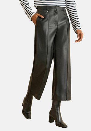 Fekete bőr culottes sima textúrával, magas derékrésszel és oldalzsebekkel, fekete magassarkú csizmával és csíkos felsővel párosítva.