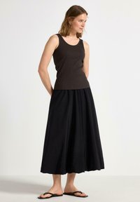 Brun ribbet tank top i kombination med en flydende sort maxi nederdel. Sættet har en afslappet pasform og blødt stof. Sorte sandaler fuldender looket.