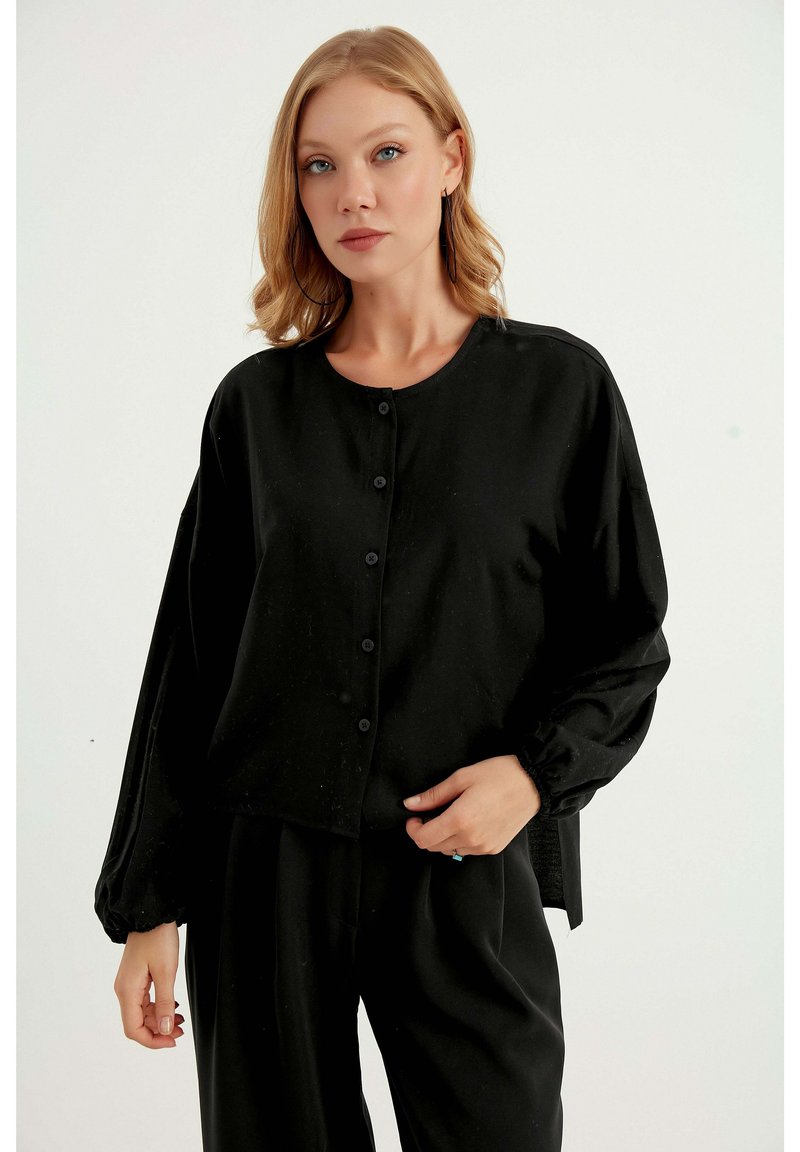 Top in tessuto leggero nero, con scollo rotondo, maniche lunghe a palloncino e chiusura con bottoni; presenta polsini elasticizzati per una vestibilità ottimale.