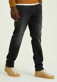 Mustad denim püksid kitsas lõikega, millel on kulunud detailid ja viis taskut. Kombe peal beežid kõrged tossud.