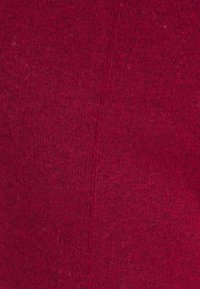 Tissu tricoté d'une couleur rouge profond avec une texture douce, présentant un motif légèrement chiné et des détails de couture visibles.