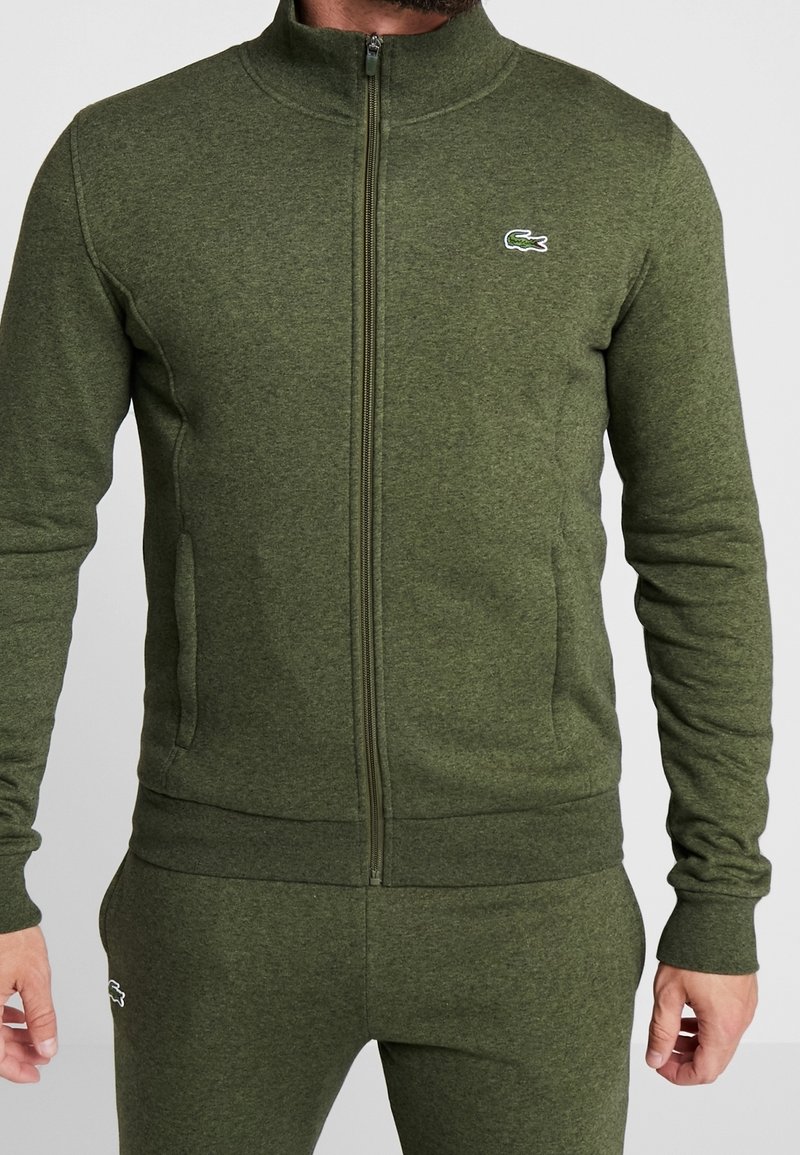 Zelená mikina na zip vyrobená z texturovaného materiálu, s vysokým límcem, předními kapsami a malým logem Lacoste na levé hrudi.