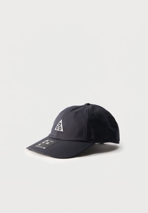 Gorra de béisbol negra con el logo triangular ACG en la parte frontal y una etiqueta en la visera curva, colocada sobre un fondo blanco liso.