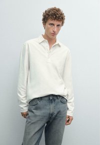 Hvid langærmet polo skjorte med tre-knaps placket, parret med lyseblå denim jeans med klassisk fem-lomme design.