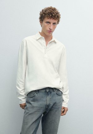 Weißes Langarm-Polohemd mit drei Knöpfen, kombiniert mit hellblauen Denim-Jeans im klassischen Five-Pocket-Design.