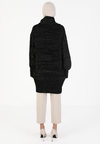 Black textured oversized sweater with a high collar, worn over light beige cropped pants and nude high-heeled shoes.