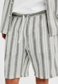 Leinen-Shorts mit vertikalen grauen und weißen Streifen, ausgestattet mit einem elastischen Bund und Kordelzug. Mittellange geschnitten mit einem lässigen Sitz.