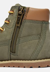Stivale verde in suede con dettagli in pelle marrone, dotato di lacci gialli e rossi, cerniera laterale e suola testurizzata per una buona aderenza.