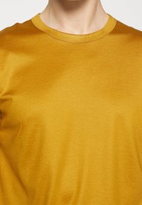 Kortärmad t-shirt med rund hals i senapsgul, tillverkad av mjukt material med en lätt lyster och minimala sömnadsdetaljer.