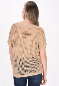 Pletený top ve světle béžové barvě s volným, otevřeným vzorem. Má krátké rukávy a široký výstřih, s texturovaným žebrováním na lemu.