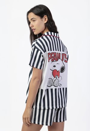 Mujer con pijama de rayas verticales en blanco y negro, con un Snoopy sosteniendo un corazón rojo y el texto "PEANUTS" en la parte trasera.