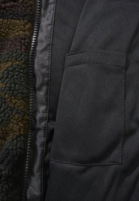 Black zippered jacket with a textured inner lining, featuring a smooth surface, mesh fabric, and a small external pocket.