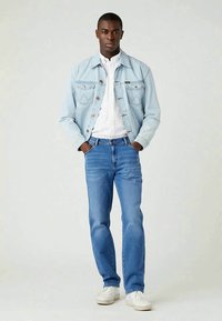 Svetlomodrá denimová bunda s gombíkovým uzáverom, pod ňou biely pás a modré džínsy, doplnené bielymi teniskami. Neformálny strih.