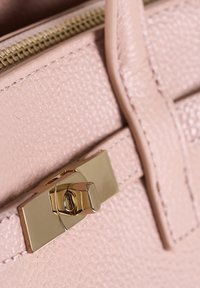 Primo piano di una borsa in pelle rosa texturizzata con una chiusura rettangolare dorata e una cerniera visibile nella parte superiore.