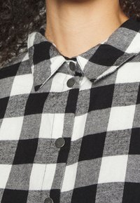 Schwarz-weißer kariert flanellhemd mit spitzem Kragen, ausgestattet mit metallischen Druckknöpfen und einem weichen, strukturierten Stoff.