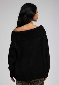 Pull en tricot noir surdimensionné avec un large col côtelé décolleté, un tissu texturé et des manches longues. Assorti à un pantalon à motifs léopard.