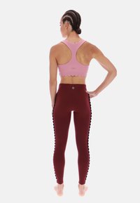 Růžová sportovní podprsenka s vlnkovým lemem ve tvaru mušle ve spojení s vínově červenými legínami s vysokým pasem, zdobenými černými vlnkami podél vnějších švů.