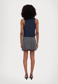 Marinblå ärmlös topp som är kombinerad med en grå plisserad minikjol. Outfiten har en figurnära design, med en slät textur och ett subtilt rutmönster.