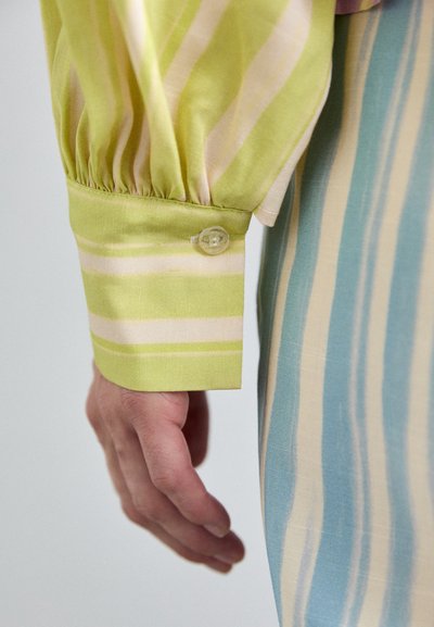 Light green striped shirt cuff with a button; silky texture; hand visible, layered with a striped blue garment.