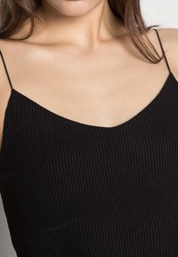 Débardeur noir côtelé avec fines bretelles, présentant un décolleté en V. Le tissu a une apparence texturée et une silhouette ajustée.