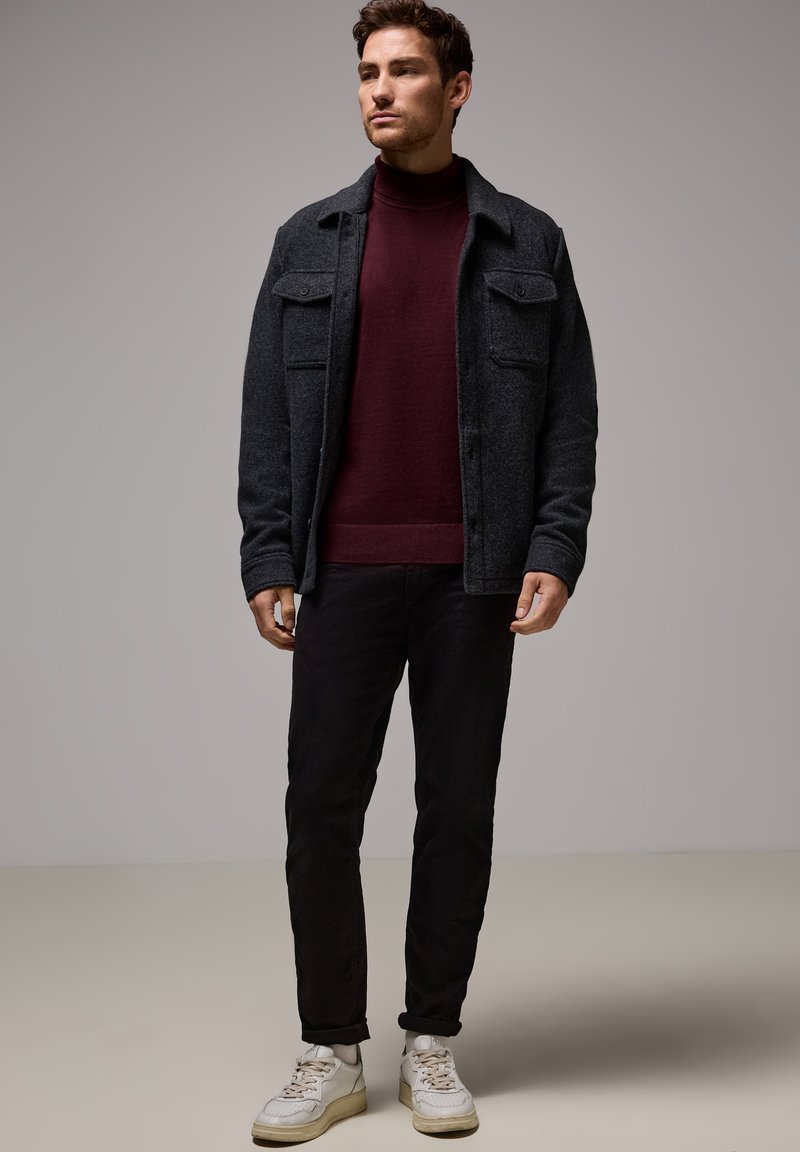 Mörkgrå ullskjortjacka, vinröd polotröja, svarta byxor och vita sneakers. Har dubbla bröstfickor och en avslappnad passform.