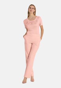 Lichtroze top met korte mouwen en een decoratief uitsnijdingspatroon, gecombineerd met bijpassende hoge broek met zijzakken en een relaxte pasvorm.