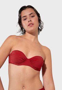 Červený bandeau bikiny vrch vyrobený z hladkej, elastickej látky s nariasením a bezšvovým dizajnom, vhodný na plavky.