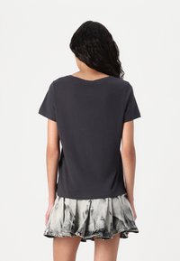 T-shirt gris foncé à manches courtes et à coupe décontractée, associé à une jupe légère à volants avec un motif décoloré.