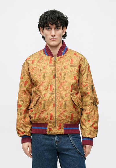 Zlatá bomber bunda so zložitými červenými a oranžovými vzormi, rebrovaným bordovým golierom a manžetami, bočnými vreckami a zapínaním na zips.