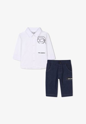 Camicia bianca a maniche lunghe con una grafica di cartone animato nera e logo, abbinata a pantaloni in denim scuro con un patch logo e tasche strutturate.