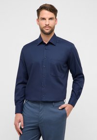 Camicia blu navy a maniche lunghe con bottoni e una tasca, realizzata in tessuto liscio. Presenta un colletto classico e bottoni neri.
