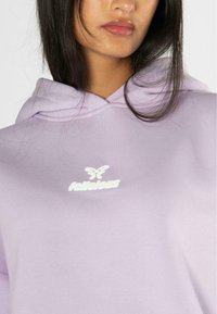 Felpa viola chiaro realizzata in tessuto morbido, con un logo bianco raffigurante una farfalla sul petto e un cappuccio classico con cordini.