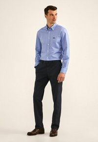 Camisa azul clara de botones con un bolsillo, combinada con pantalones oscuros de color marino y zapatos de cuero marrón. Diseño simple, textura de tela nítida.